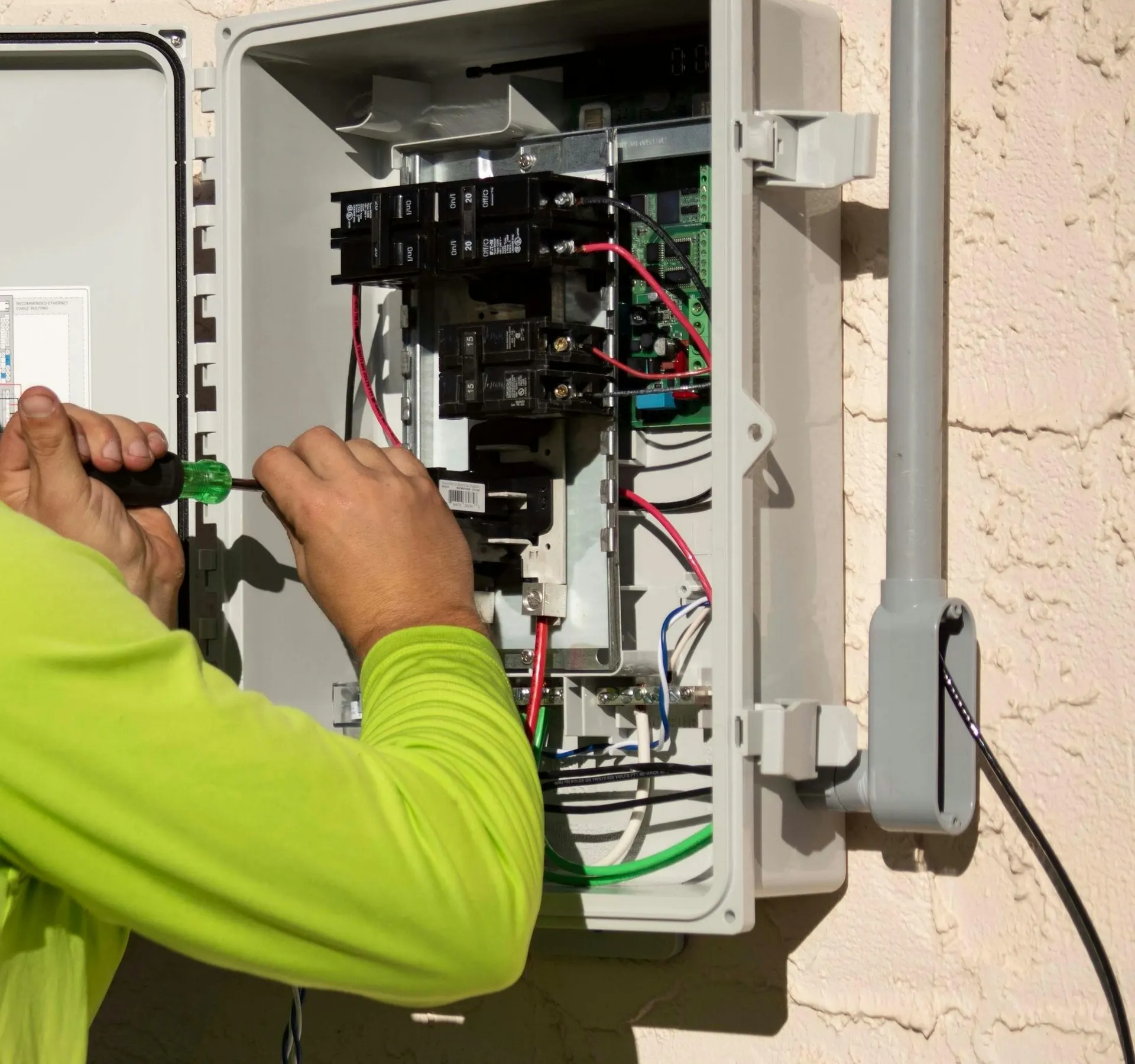 Mãos de eletricista com chave de fenda dentro de um quadro de disjuntores aberto